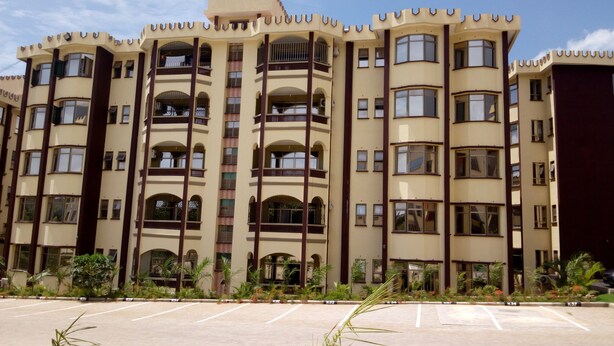 A multi-story hotel with balconies, a parking lot, and landscaping. - Sunset Paradise Baringo 11 (Shanzu)