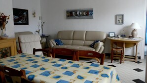 A living room with a sofa, a dining table with a blue and white tablecloth, a small round table with a lamp, and a chair. - Country house with enclosed garden (La cotinière Saint-Pierre-d'Oléron)