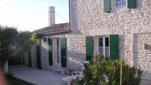 A stone building with green shutters, a tiled roof, and a small garden area with a bench and plants. - Country house with enclosed garden (La cotinière Saint-Pierre-d'Oléron)