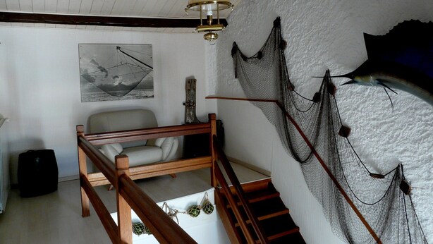 A room with a wooden staircase, a white couch, a hanging lamp, and a wall with fishing nets. - Country house with enclosed garden (La cotinière Saint-Pierre-d'Oléron)