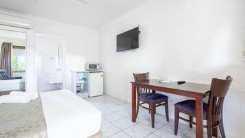 A hotel room with a bed, a desk, a chair, a television, and a bathroom visible through an open door.