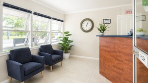 A hotel reception area with a clock, a plant, and two armchairs.