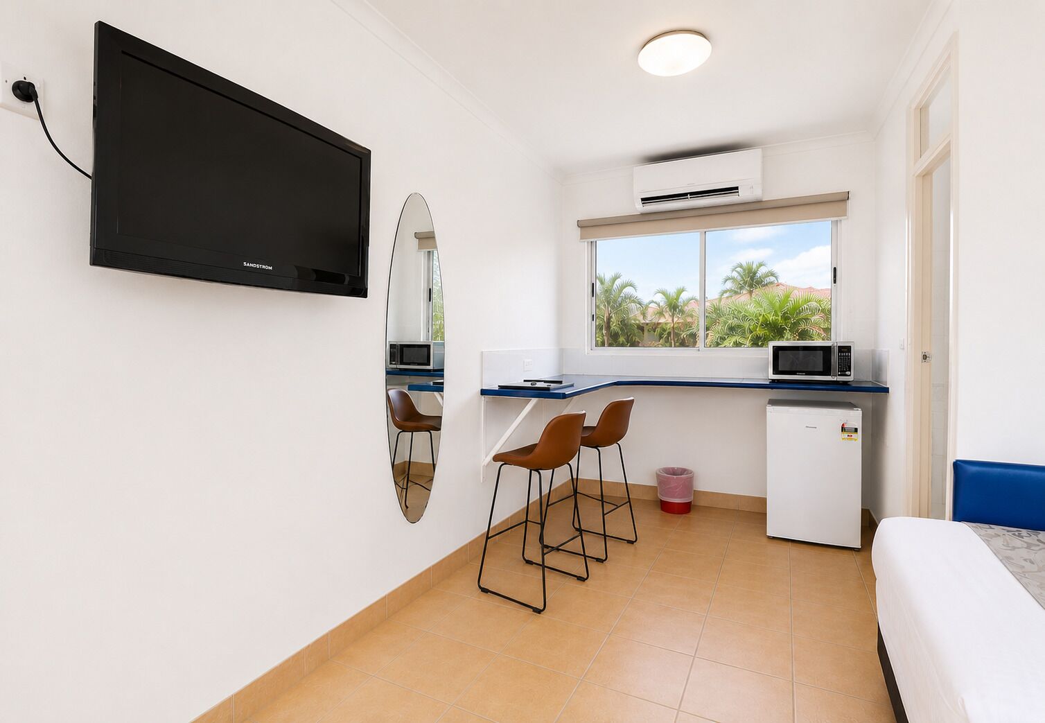 A compact room with a TV, a microwave, a small fridge, a window with a view, and a bed.