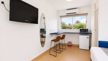 A compact room with a TV, a microwave, a small fridge, a window with a view, and a bed.