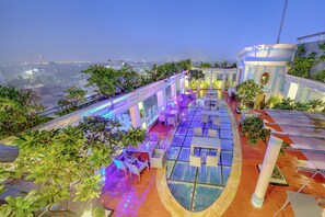 A rooftop terrace with glass balustrades, outdoor seating, and a view of the cityscape. - De Sovrani (Bidhannagar)