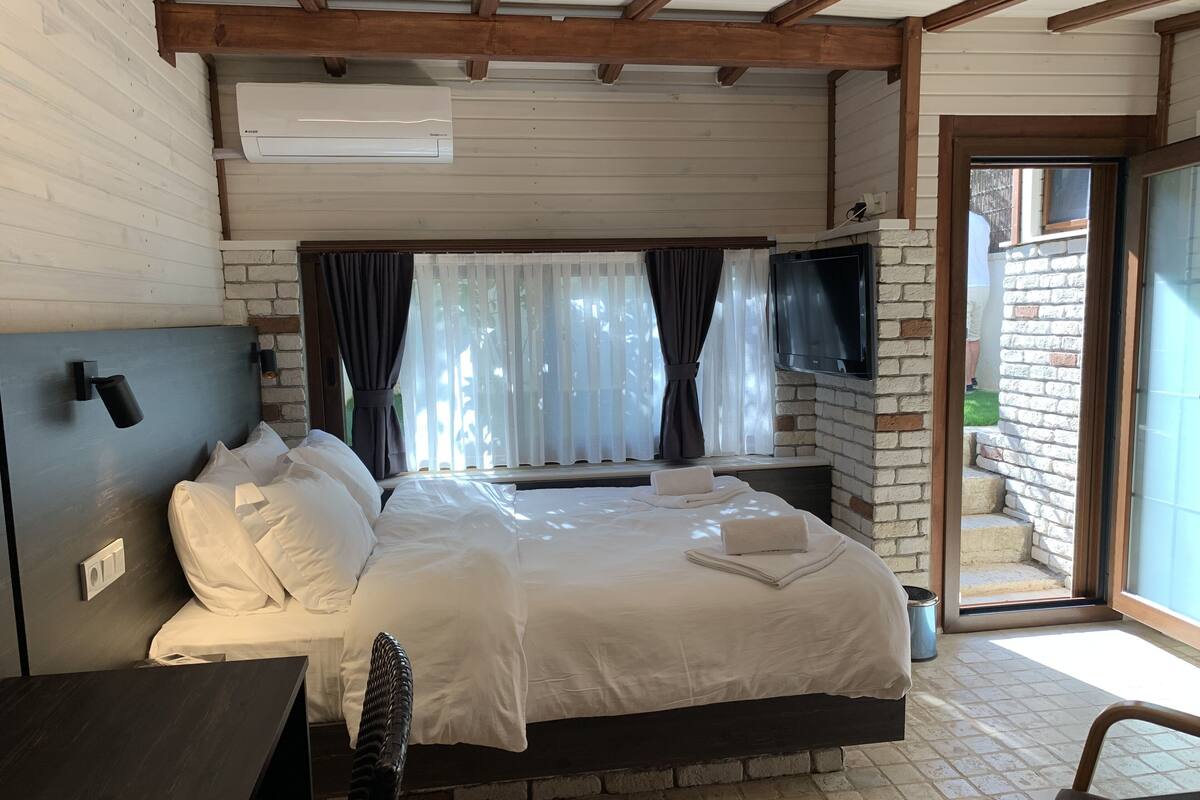 A bedroom with a bed, bedside tables, a TV, and a window with curtains.