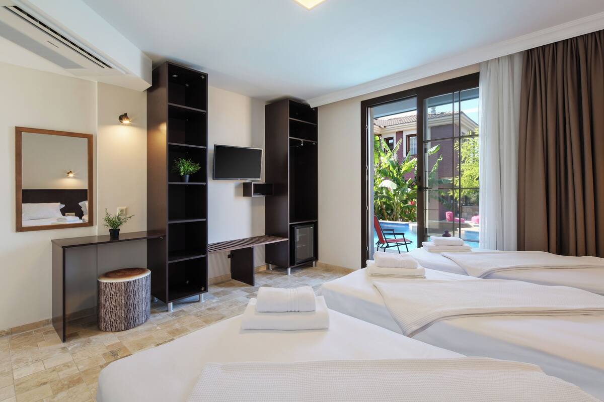 A hotel room with two beds, a desk, a TV, and a large window with curtains.