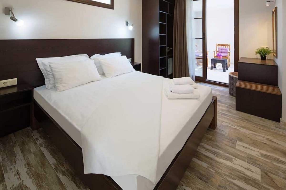 A neatly made bed with white linens, a wooden headboard, and a nightstand with a lamp.
