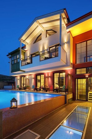 Una casa a due piani con piscina, area salotto esterna e un balcone.