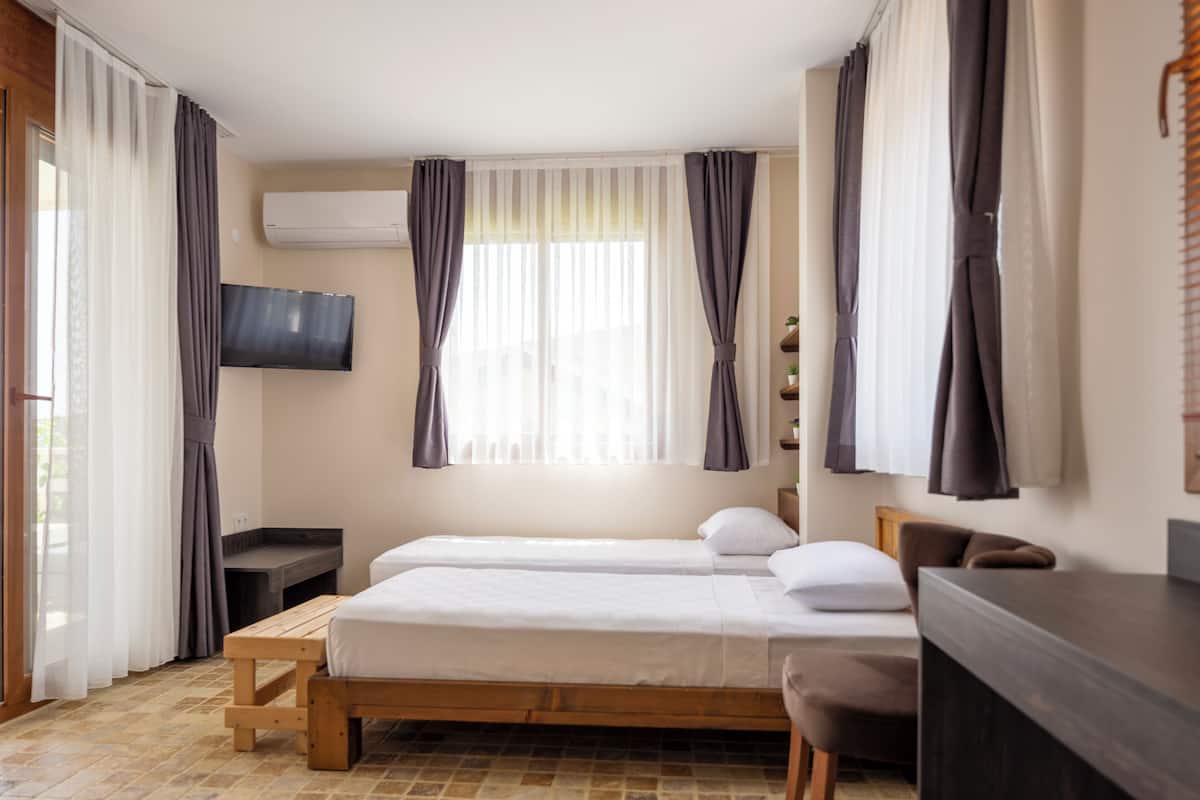 A hotel room with two beds, a desk, a TV, and a window with curtains.