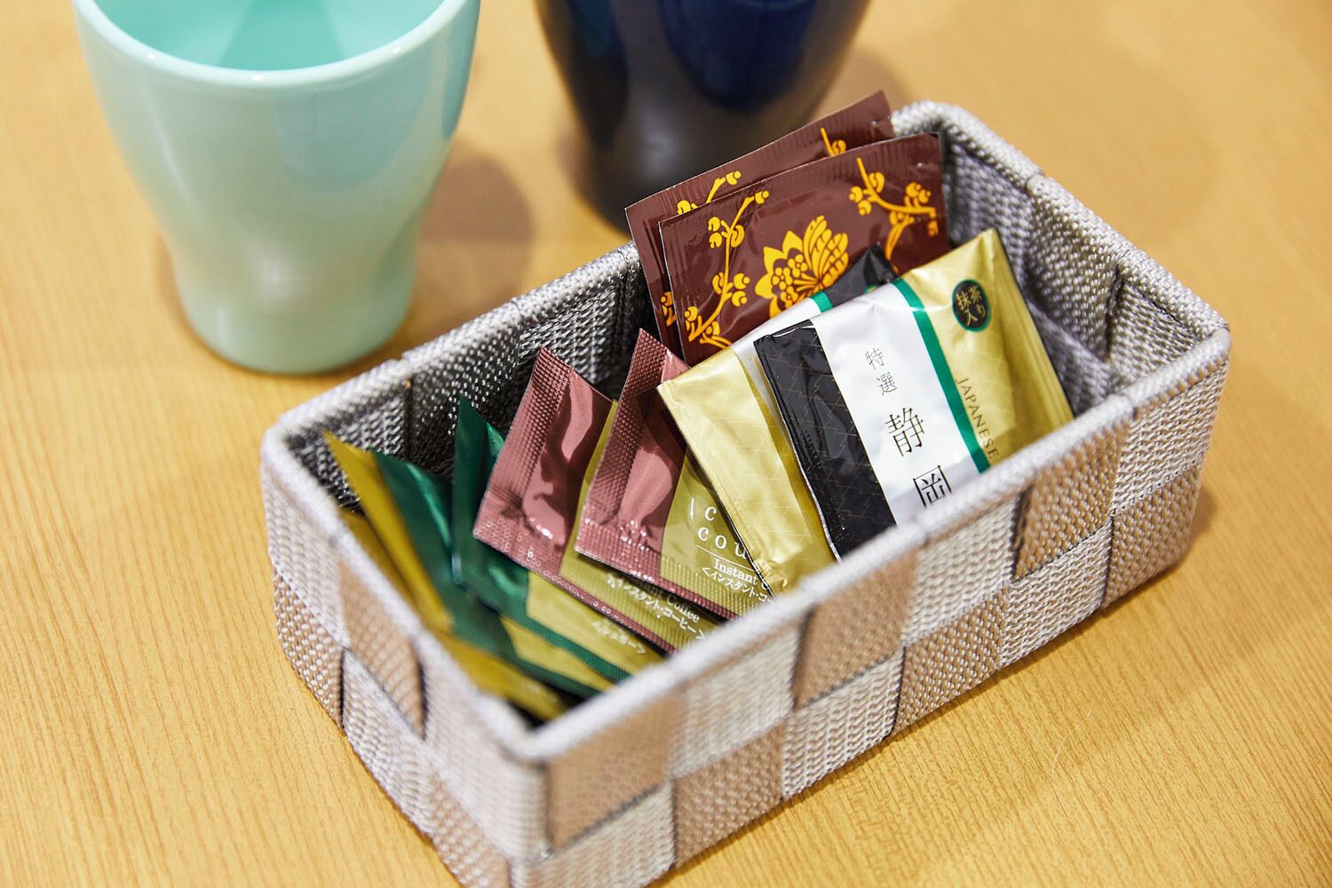 A woven basket containing various instant coffee packets on a wooden surface.