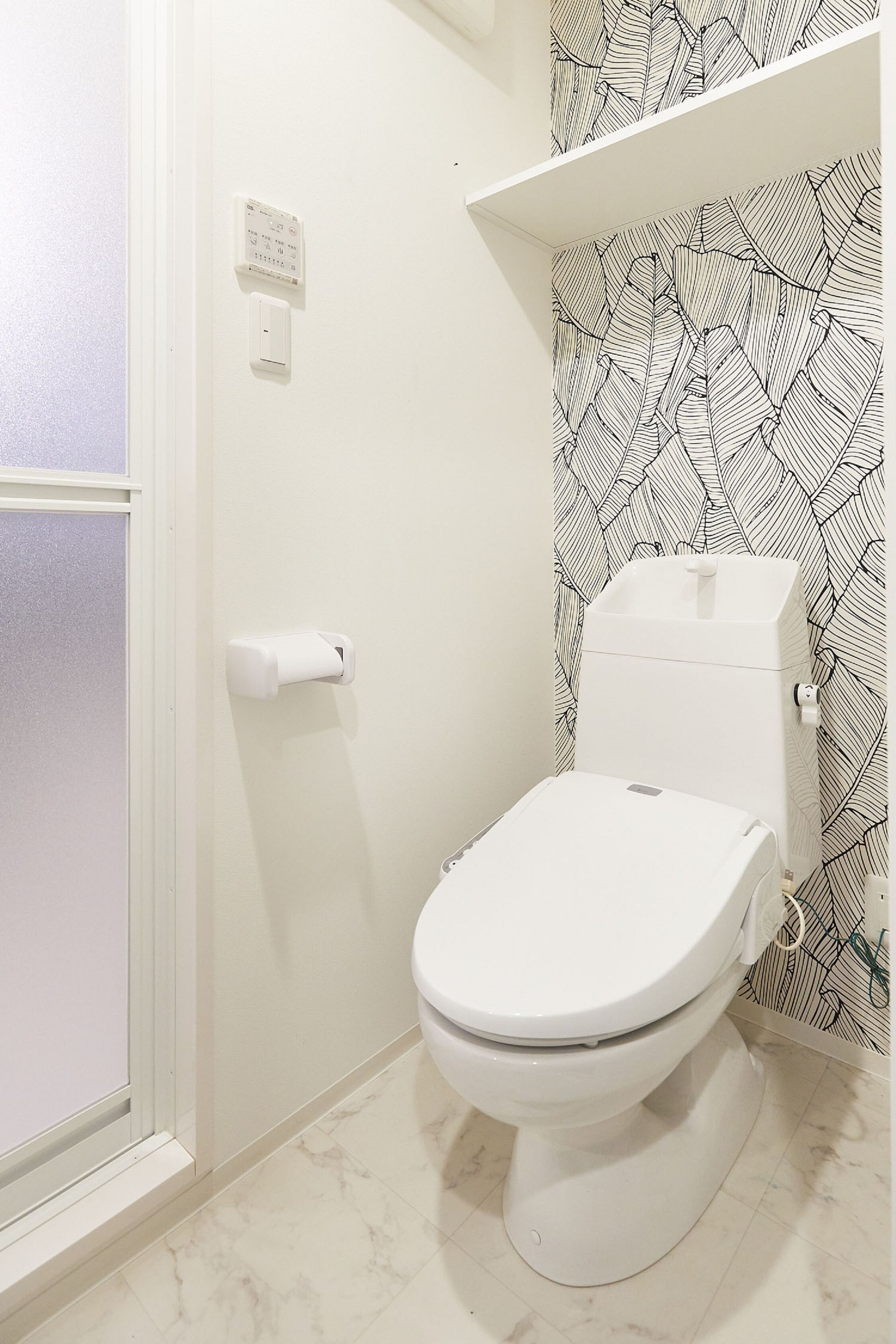 A bathroom with a toilet, a paper towel dispenser, and a wall-mounted electrical outlet.