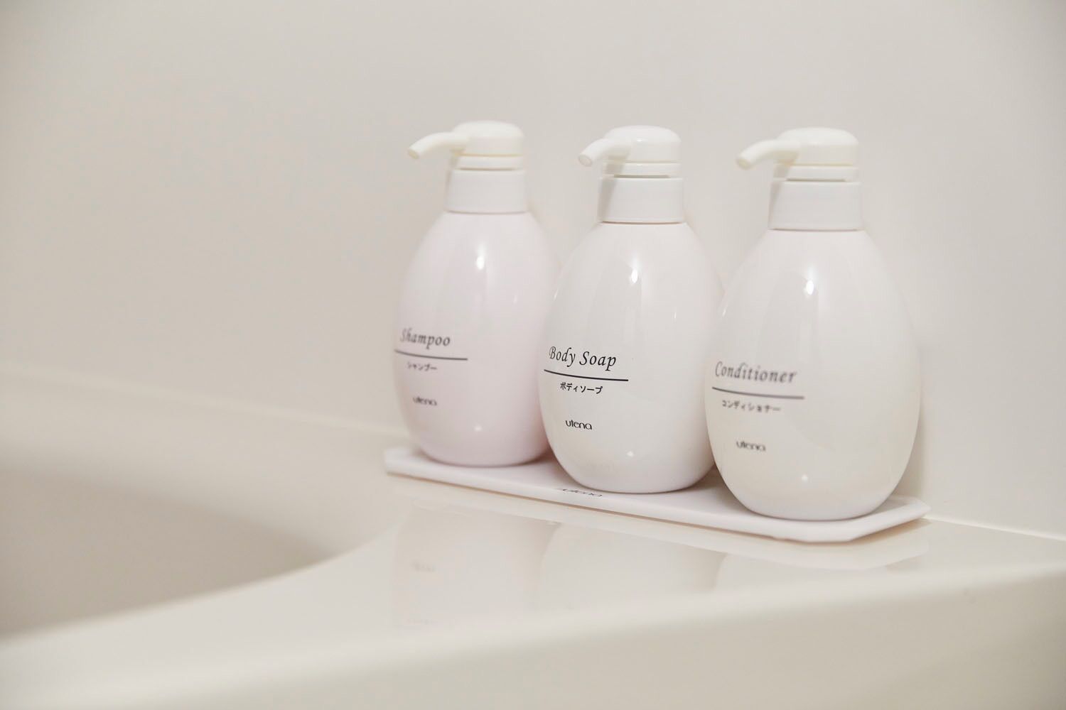 Three white bottles of shampoo, body soap, and conditioner on a white surface.