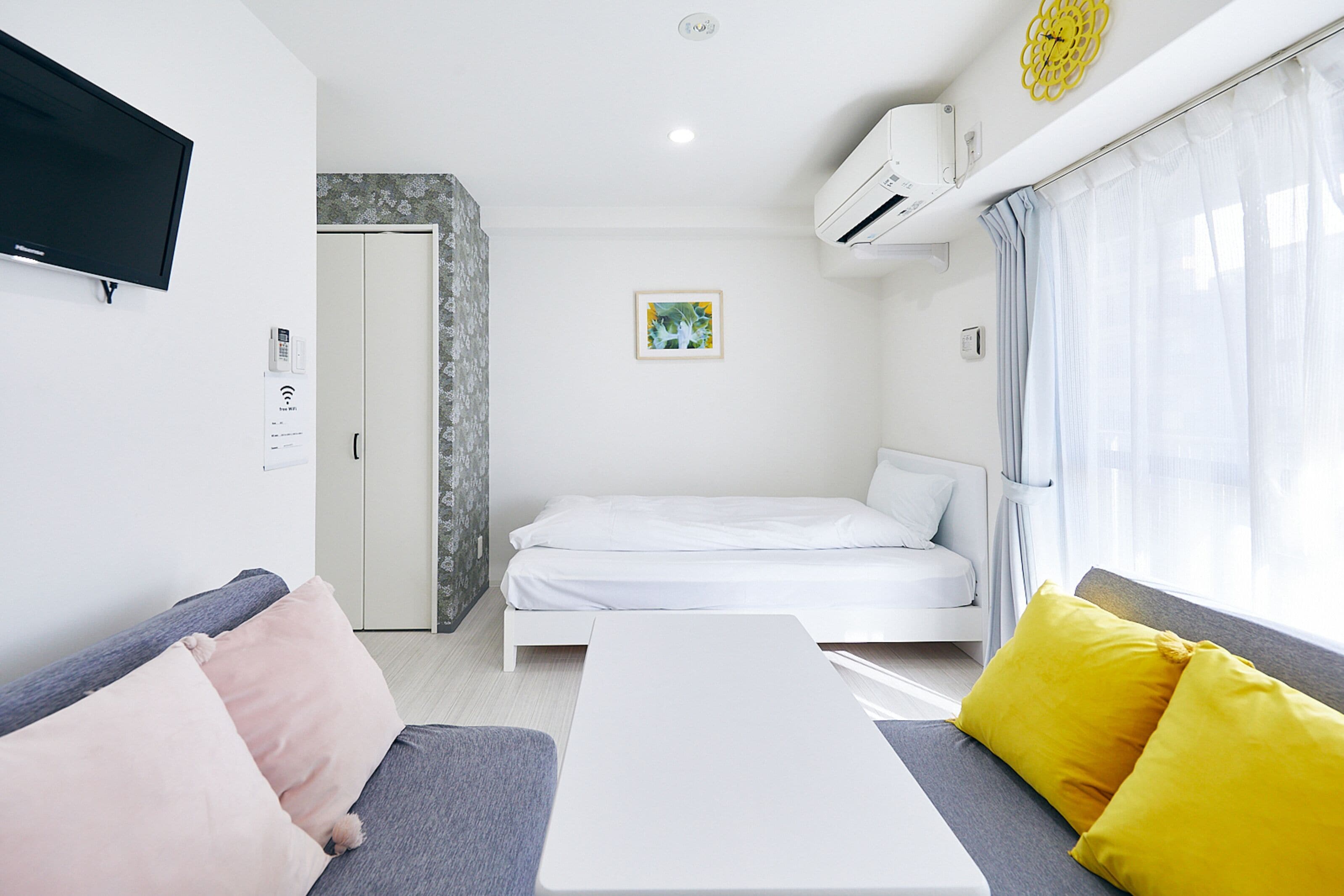 A modern room with a sofa, a bed, a TV, and an air conditioning unit.