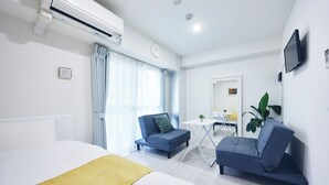 A modern hotel room with a bed, two sofas, a small table, a TV, and an air conditioning unit.