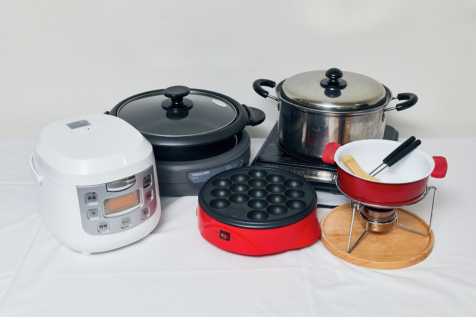 A kitchen setup with a rice cooker, a pressure cooker, a steamer, a wok, and a pot.