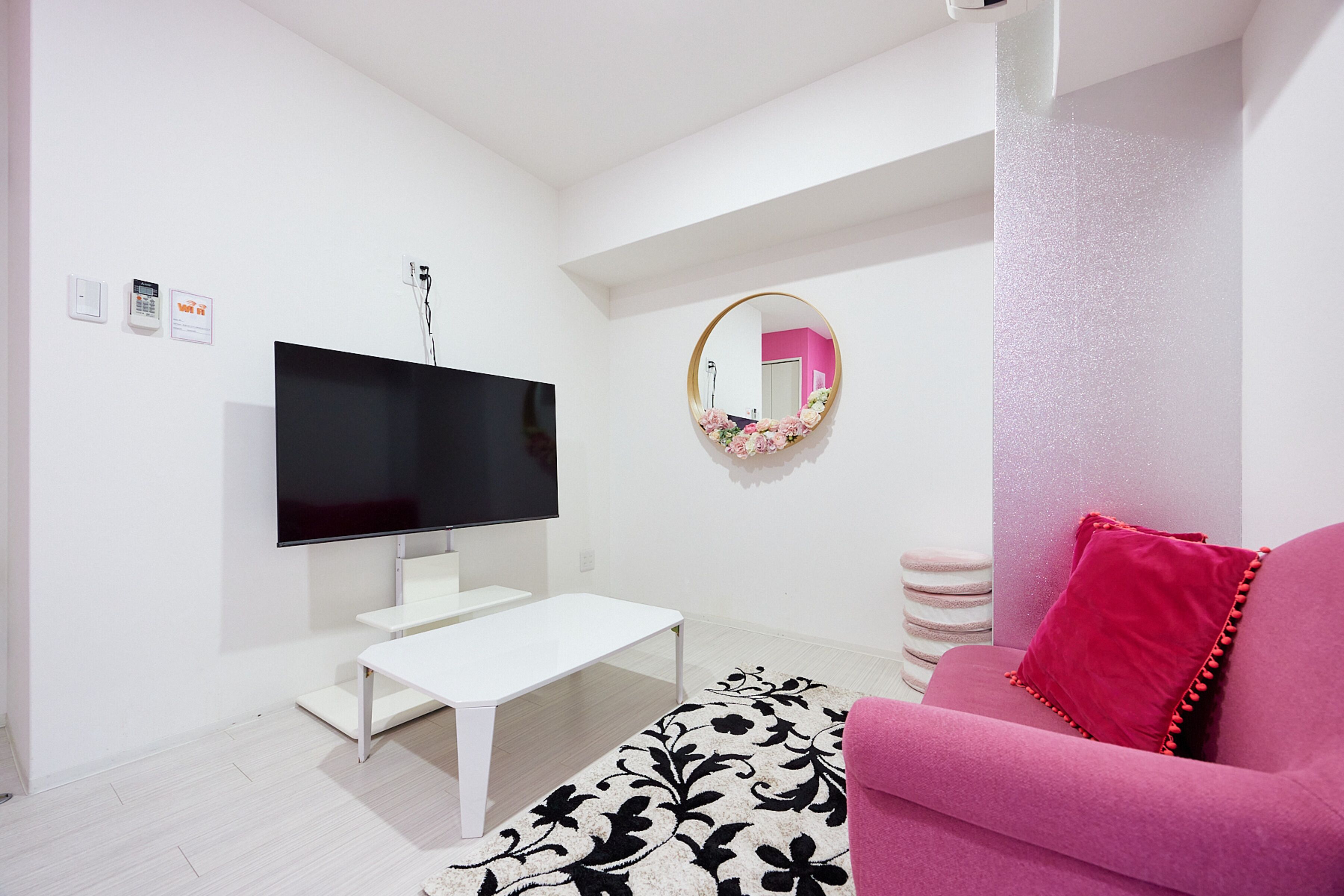 A modern living room with a flat-screen TV, white coffee table, pink sofa, and a decorative mirror.