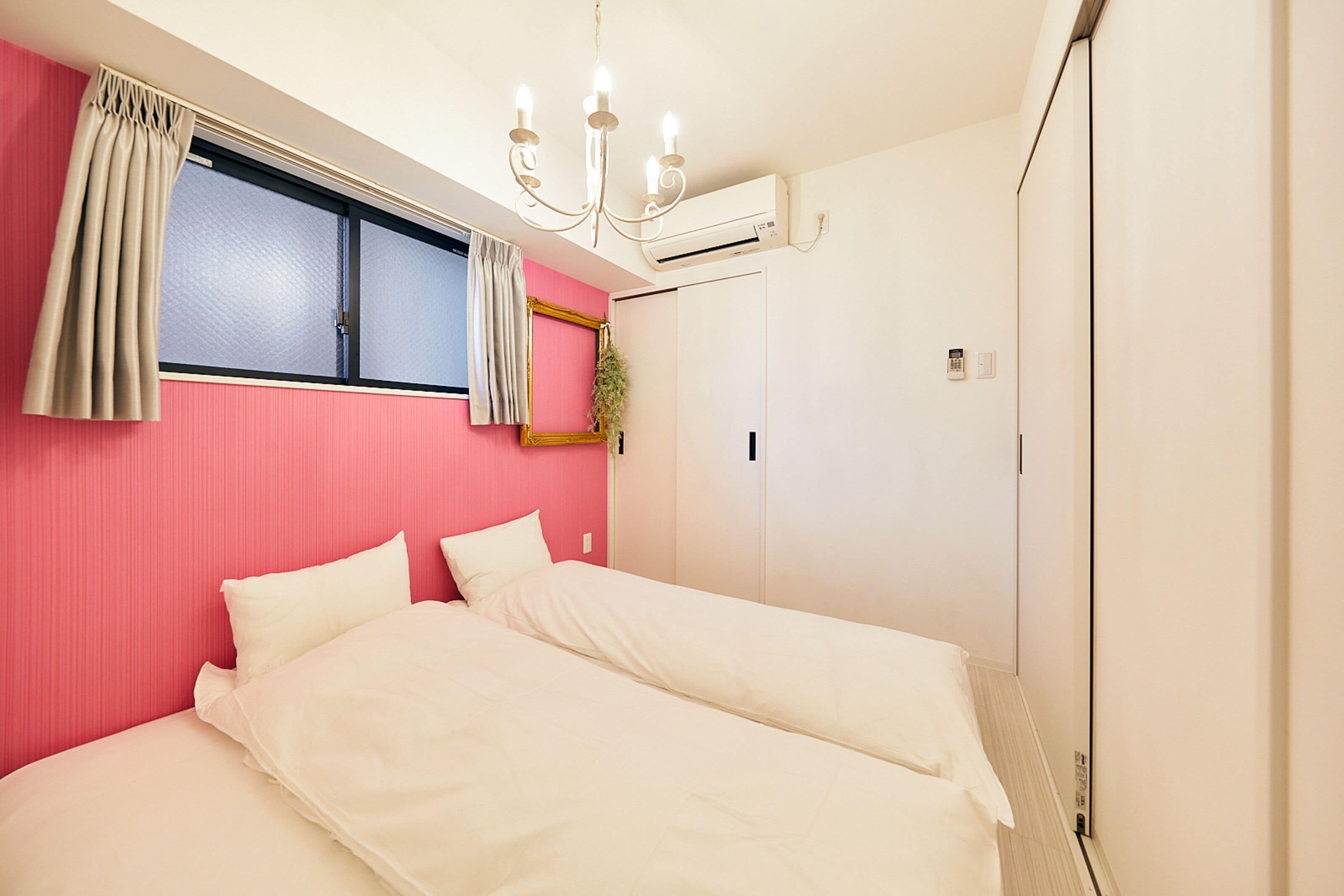 A bedroom with a bed, a window with curtains, an air conditioning unit, and a door.