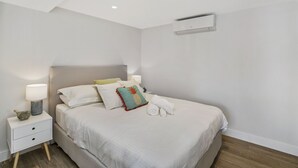 A bedroom with a bed, nightstands, a lamp, and an air conditioning unit. - Balmoral Cabana - only 150m to Balmoral Beach (Mosman)
