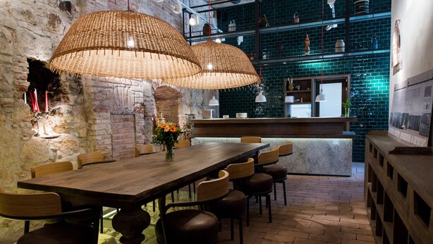 A restaurant with a long wooden table, multiple chairs, wicker pendant lights, a brick wall, and a tiled backsplash. - Guest House 1568 (Cluj-Napoca)