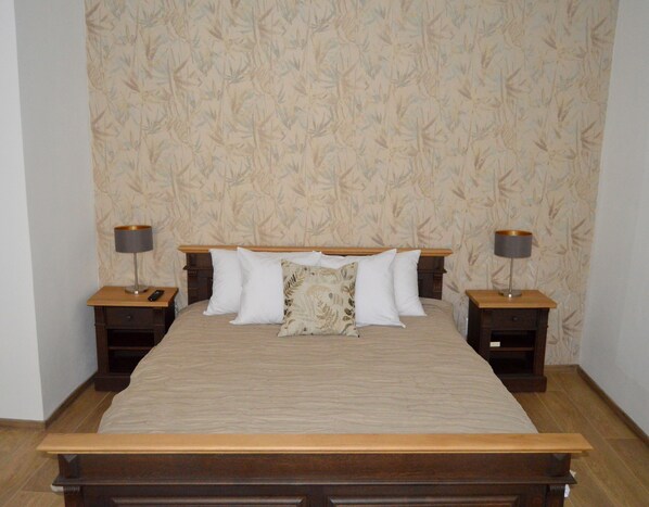 A neatly made bed with a wooden headboard, two bedside tables with lamps, and a patterned wallpaper.