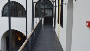 A corridor with a black floor, white walls, and a wooden railing. There are arched windows and a door at the end. - Guest House 1568 (Cluj-Napoca)