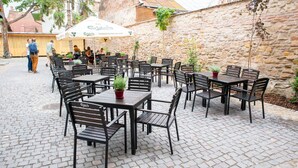 An outdoor café with stone walls and cobblestone flooring, featuring black metal tables and chairs. - Guest House 1568 (Cluj-Napoca)