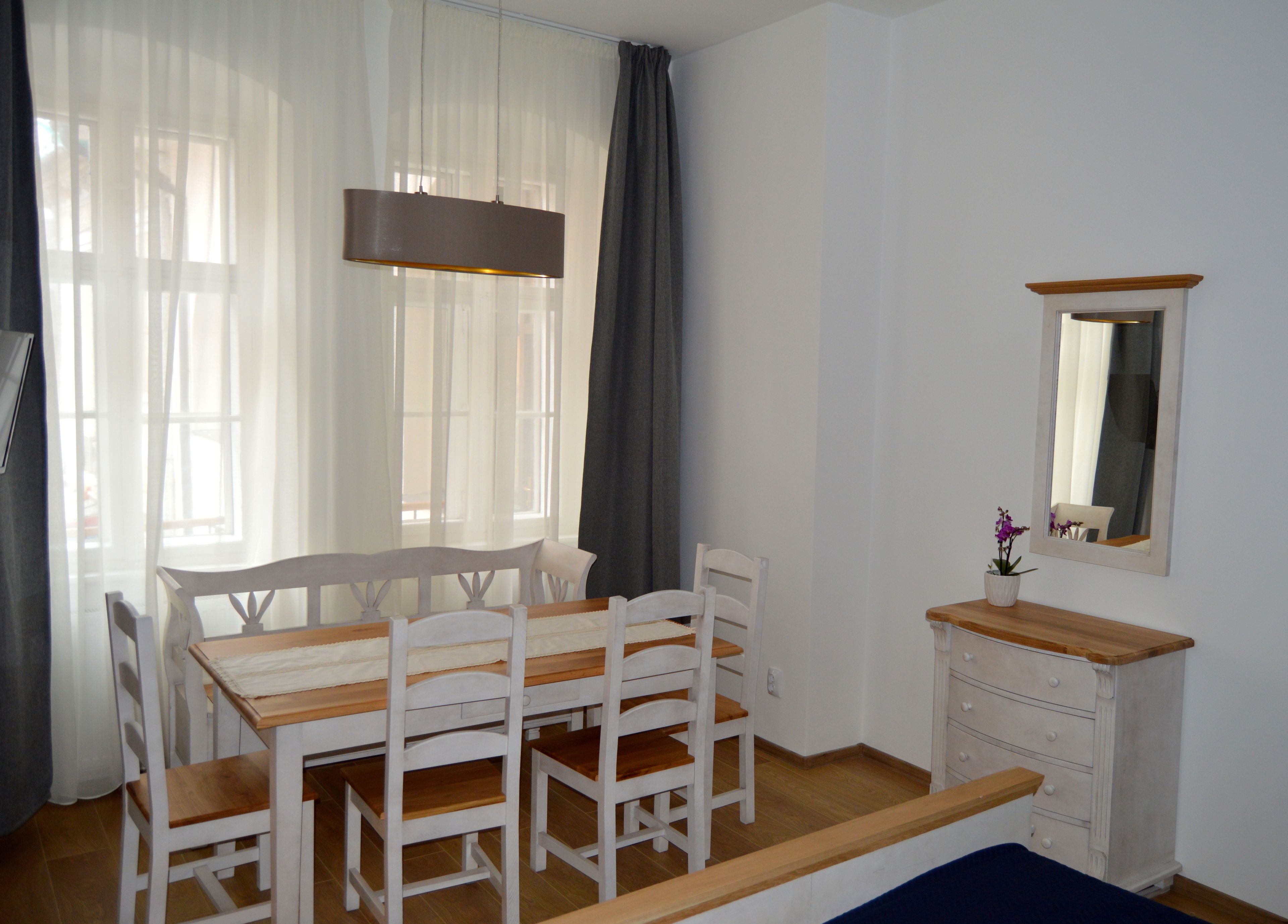 Una habitación con una mesa y sillas de madera, un aparador blanco, un espejo y cortinas translúcidas.