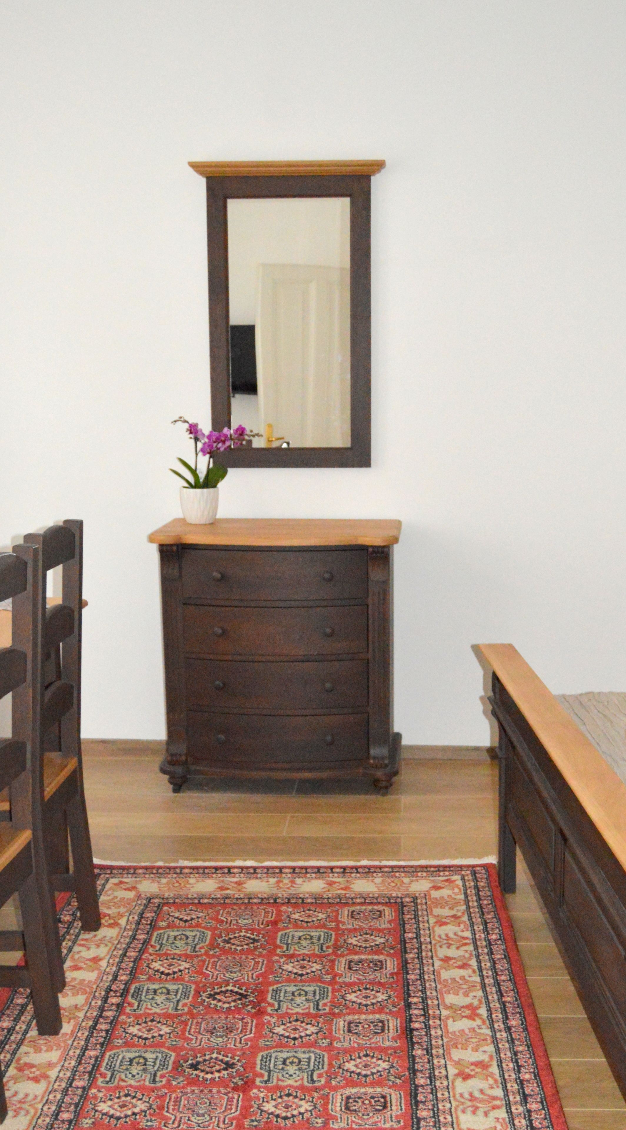 A room with a wooden dresser, a mirror above it, a chair, and a bed with a wooden headboard.