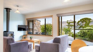 Un salon moderne avec un mur en pierre, une cheminée, un téléviseur et une grande fenêtre donnant sur les montagnes.