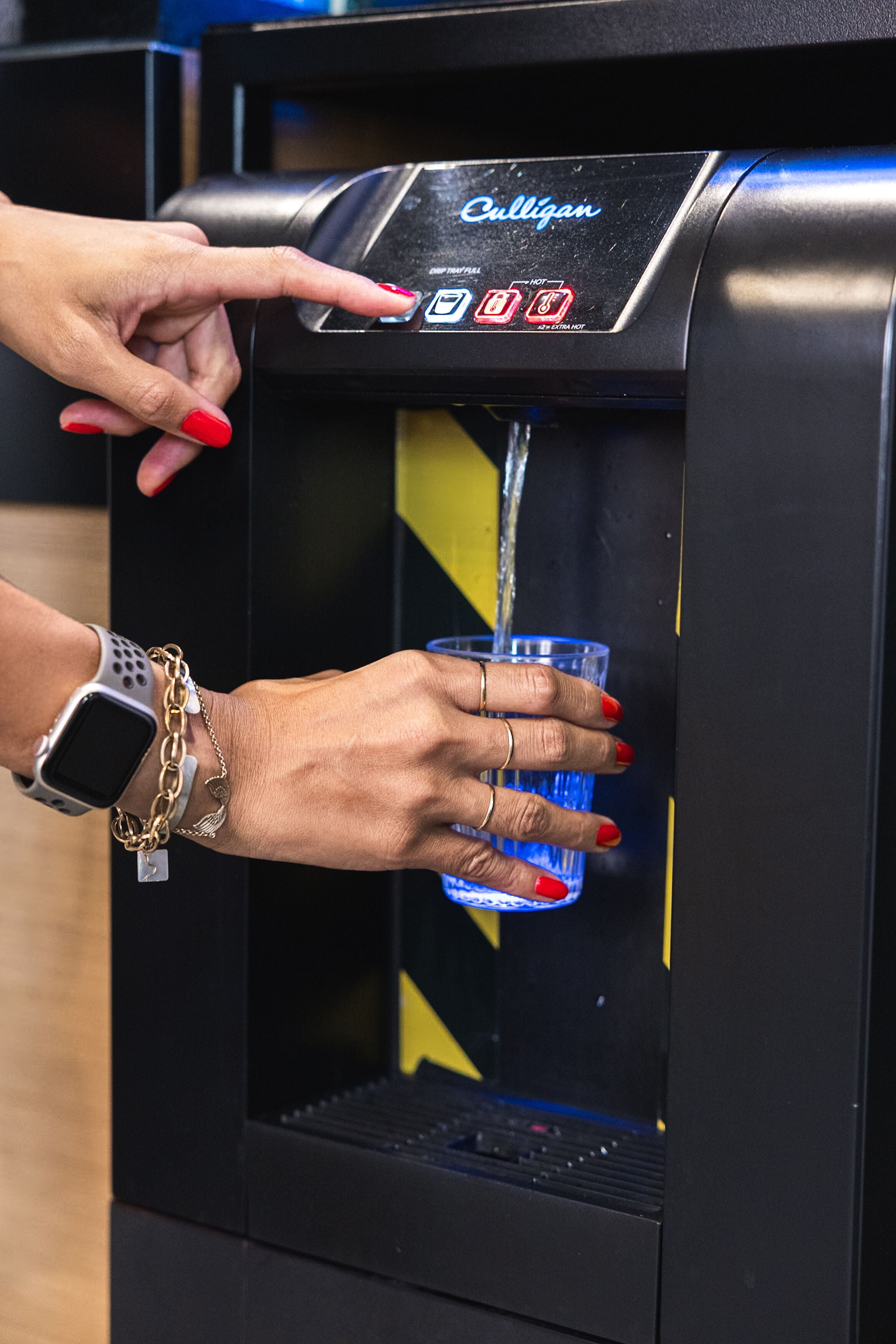 Eine Person bedient einen Wasserspender mit digitaler Anzeige und verschiedenen Wasseroptionen.