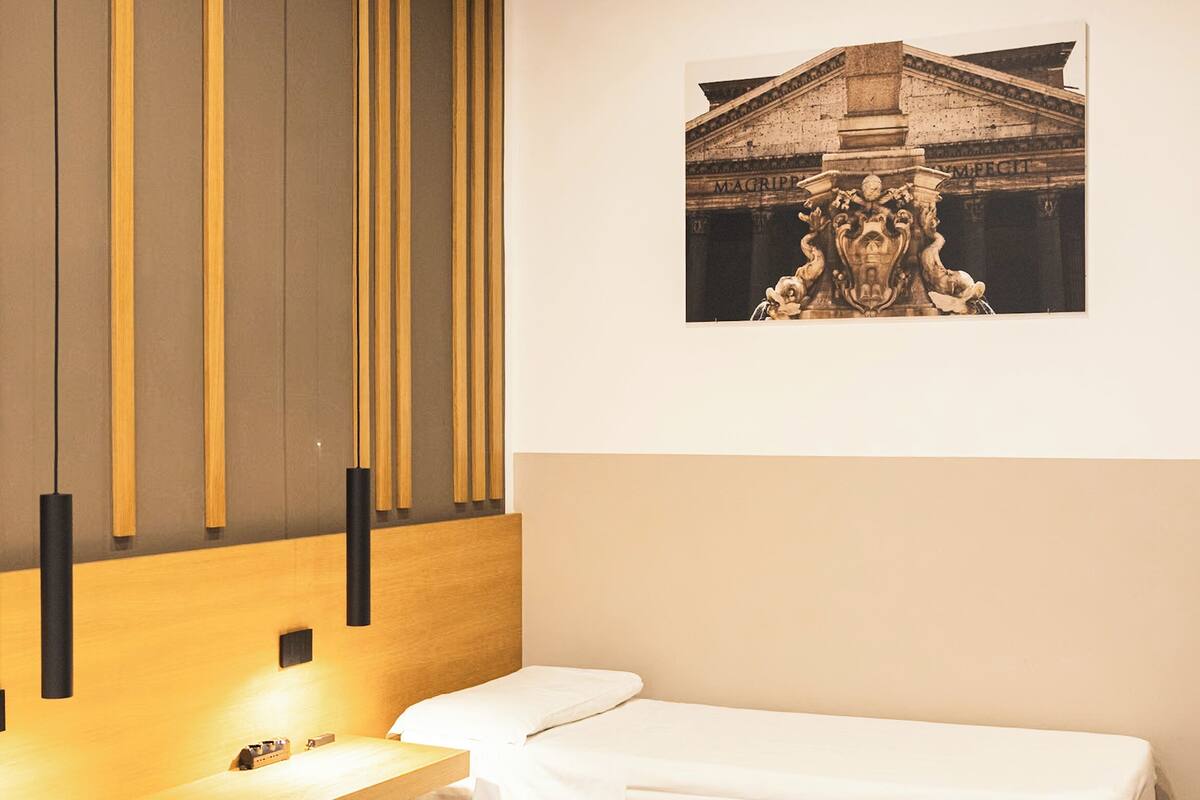 A hotel room with two beds, a wooden headboard, a bedside table, and a wall-mounted picture.