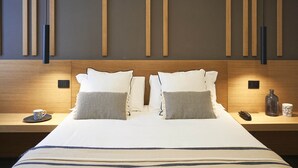 A neatly made bed with two pillows, a bedside table with a phone and a bottle, and a wall with vertical wooden panels and a hanging light fixture. - Hotel Central Lodge (Rome)