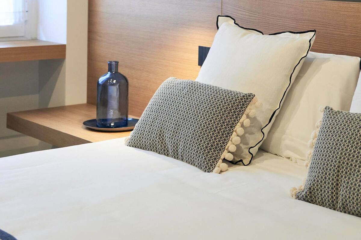 A neatly made bed with a wooden headboard, a bedside table with a glass object, and a wall with vertical wooden panels.