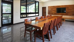 Una amplia sala de conferencias con una larga mesa de madera y sillas, un ventanal grande y un televisor montado.