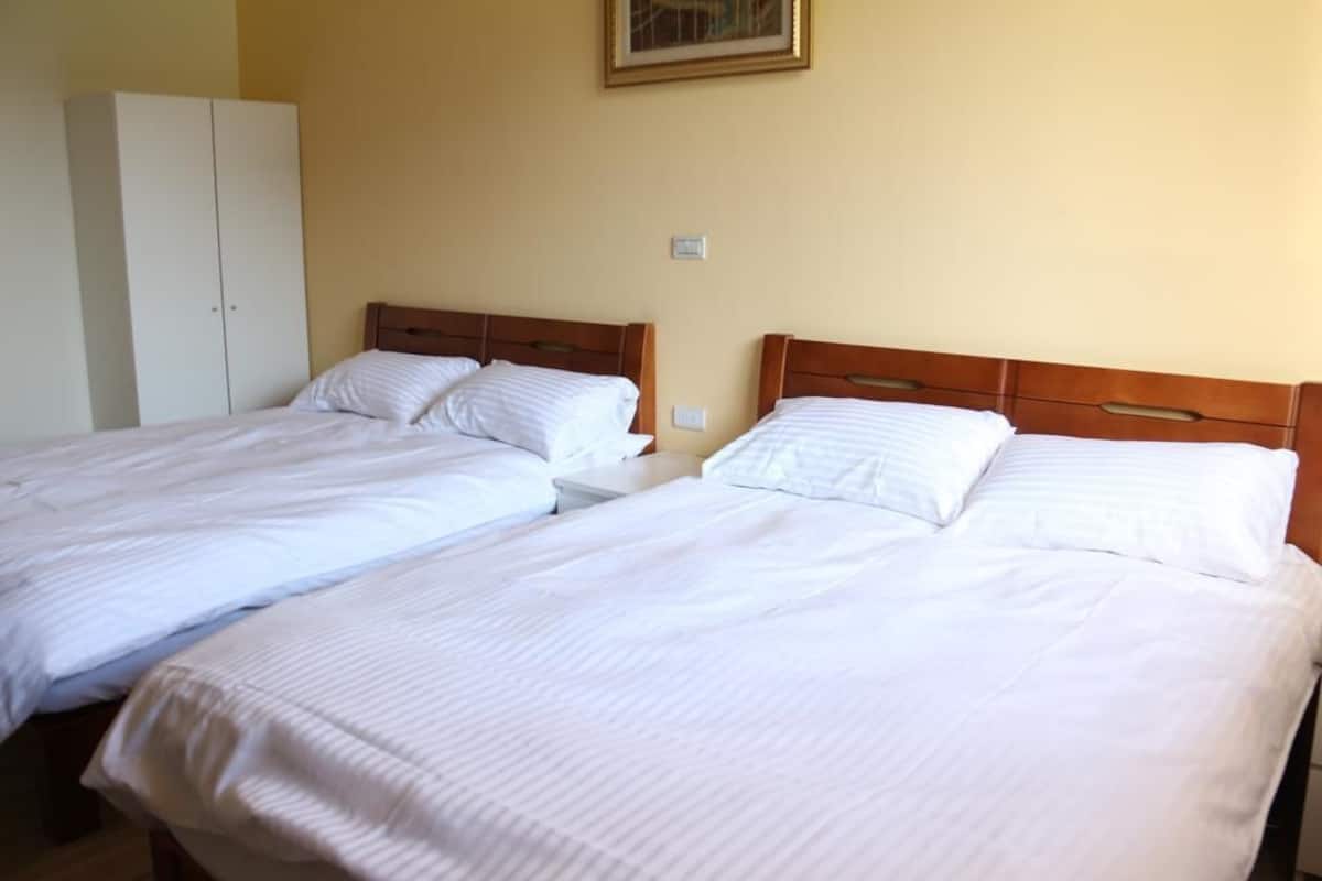 A room with two single beds, a wardrobe, and a painting on the wall.