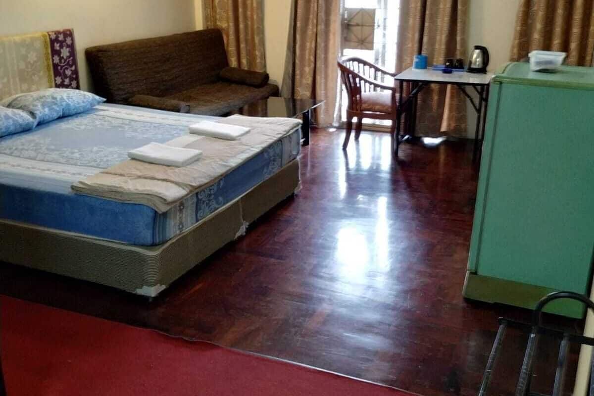A hotel room with a bed, a desk, a chair, and a green cabinet.