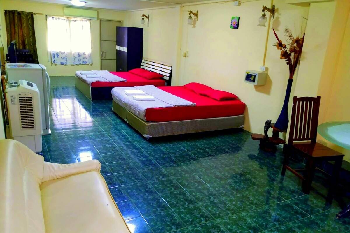 A hotel room with two beds, a desk, a chair, a small table, a cabinet, and a decorative plant.