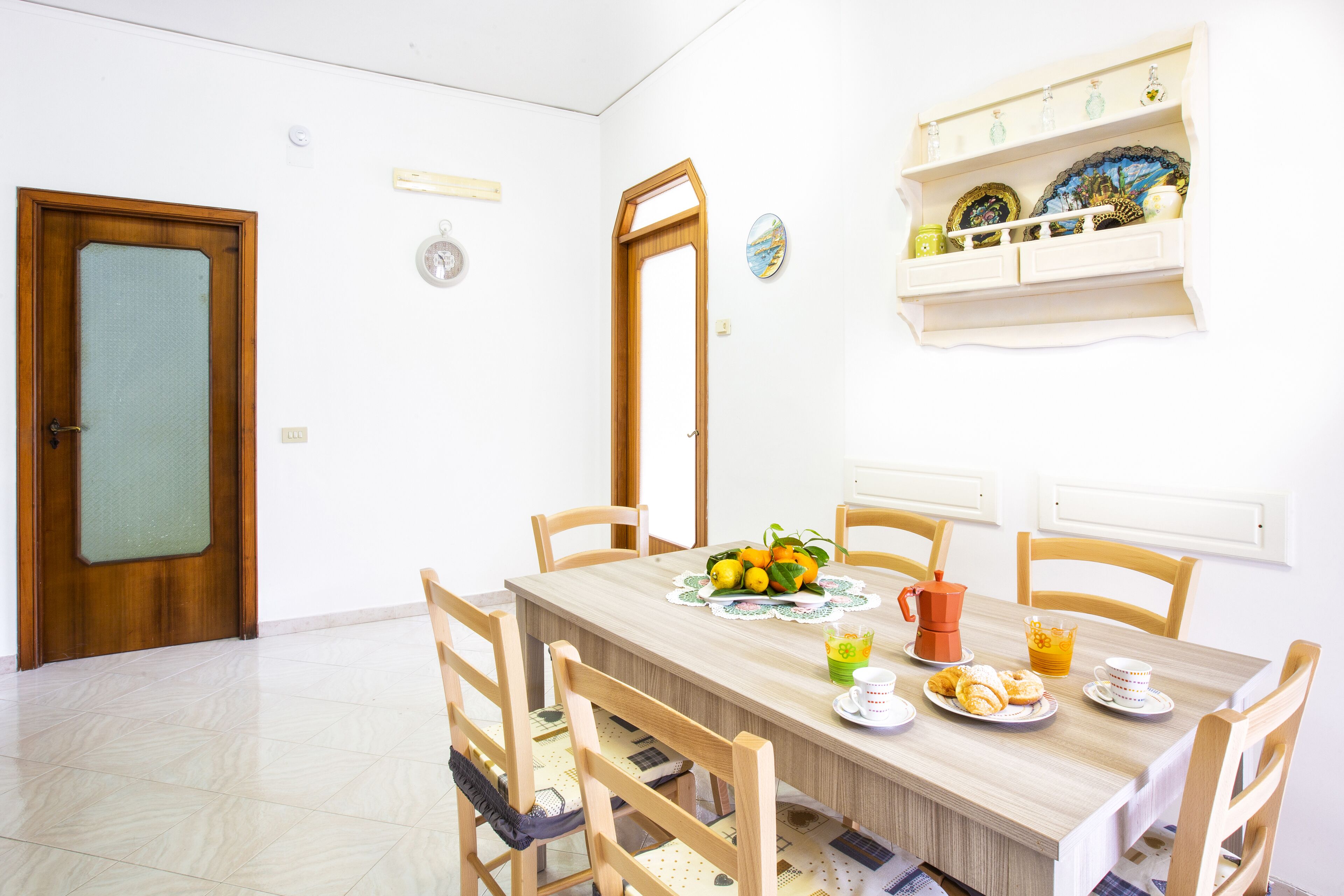 A dining area with a wooden table, chairs, and a breakfast setting including fruits, coffee, and tea.