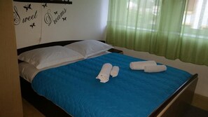 Una cama con una colcha azul, dos almohadas blancas y dos toallas enrolladas.