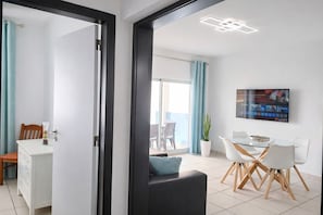 A modern living room with a dining area, a TV mounted on the wall, and a balcony visible through the door.