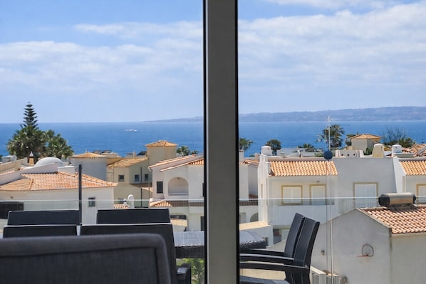 Vista desde un balcón sobre un pueblo costero con edificios de tejas rojas y un mar azul cristalino.