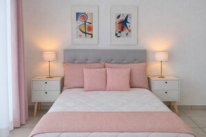 Ein Schlafzimmer mit einem Bett, zwei Nachttischen, zwei Wandlampen und zwei abstrakten Bildern.