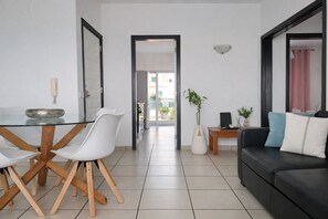 A modern living room with a black sofa, white chairs, a glass dining table, and a potted plant.