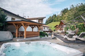 Een hottubgedeelte met houten pergola’s, lounge stoelen en een zwembadterras.