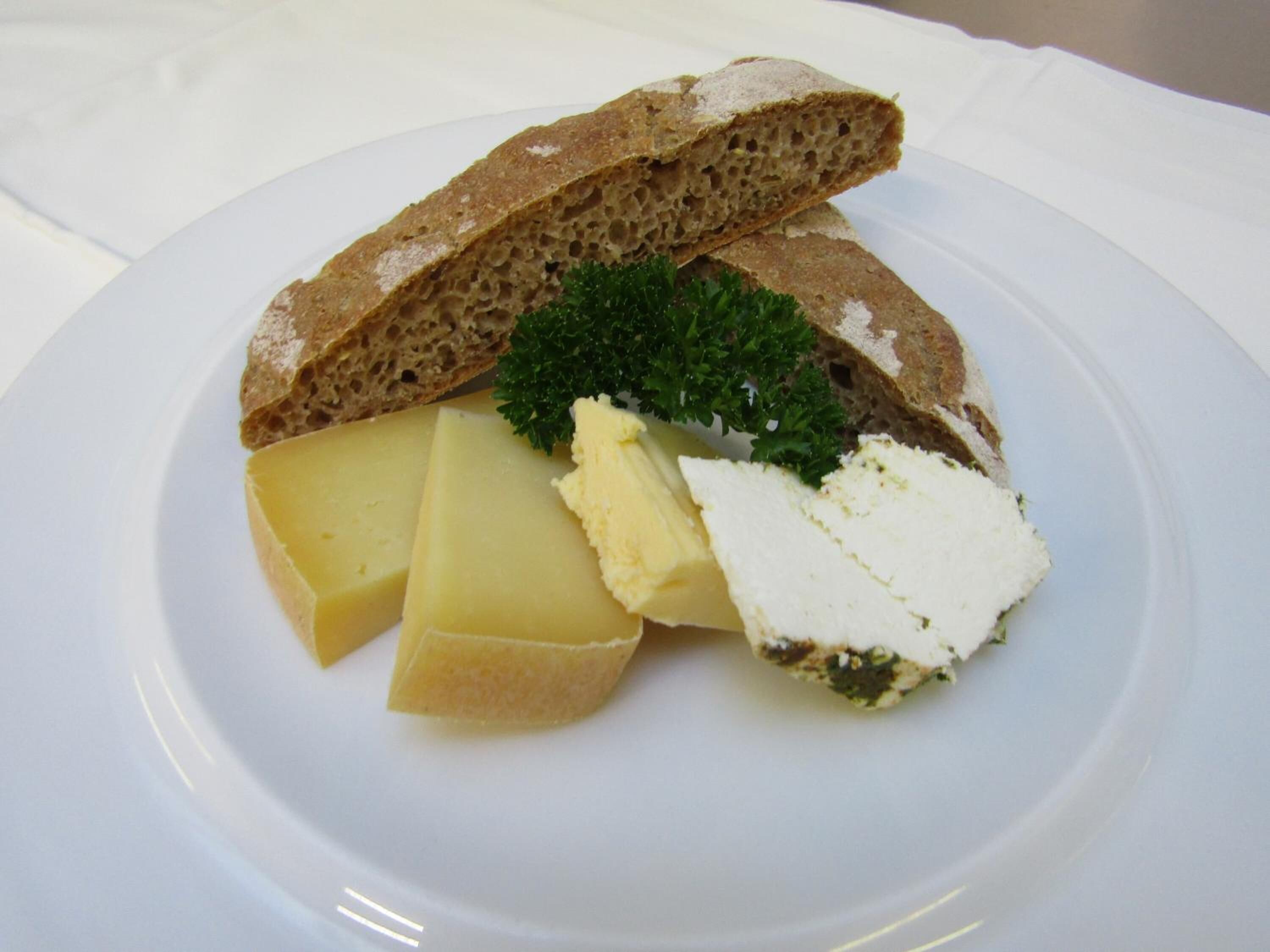 A plate with slices of cheese, a piece of butter, and a sprig of parsley.