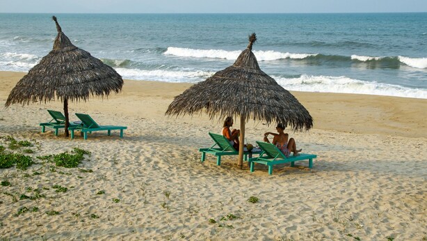 A beach with two thatched umbrellas and green lounge chairs. - Hoi An Blue Seaside Homestay (Da Nang)