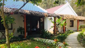 A bungalow with a thatched roof, a garden with red flowers, and a paved pathway. - Hoi An Blue Seaside Homestay (Da Nang)