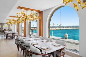 A restaurant with tables set for dining, large windows with a view of the sea, and decorative golden elements hanging from the ceiling. - Hotel Albatros Citadel (Sahl Hasheeh)