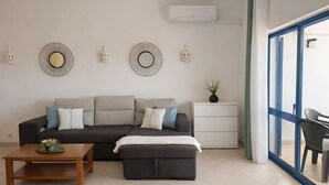 Un saló modern amb un sofà modular, una taula de centre de fusta, una taula auxiliar blanca amb un vas i elements decoratius penjats a la paret.